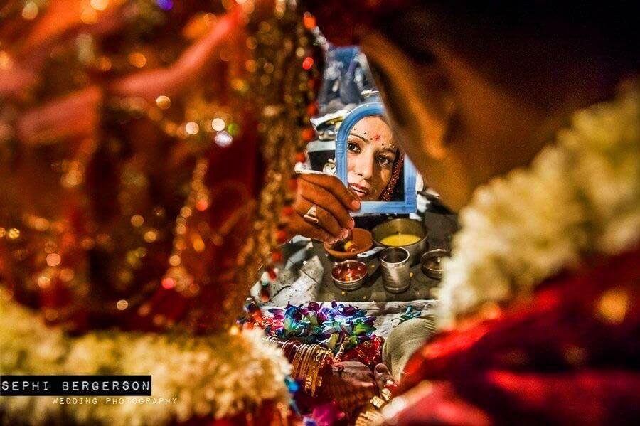 During a Kashmiri Pundit wedding I saw the priest holding a plastic miror in his hand. I had a feeling it was going to be used for the bride and groom to look at each other so quickly positioned myself just behind them and was ready as the priest held his hand out just for a second in front of the couple. It is one of those shots that one can never get unless you wait for them to happen. (Anuradha & Nikhil's Kashmiri Pundit wedding in Delhi)
